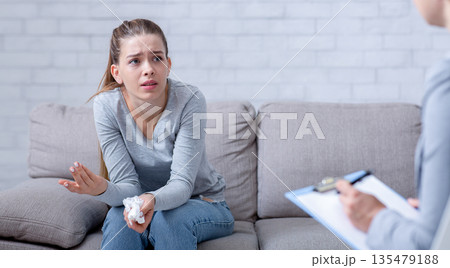 Psychological help service. Depressed female patient having psychotherapy session with counselor at office. Young woman with emotional or family problems consulting mental health professional Psychological help service. Depressed female patient having psychotherapy session with counselor at office. Young woman with emotional or family problems consulting mental health professional 135479188