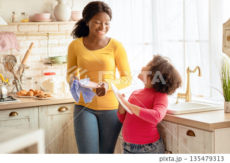 Little Black Girl Wiping Dishes Together With Mom In Kitchen, Cute Preschooler Female Child Helping Her African American Mother With Household, Enjoying Spending Time At Home, Free Space Little Black Girl Wiping Dishes Together With Mom In Kitchen, Cute Preschooler Female Child Helping Her African American Mother With Household, Enjoying Spending Time At Home, Free Space 135479313