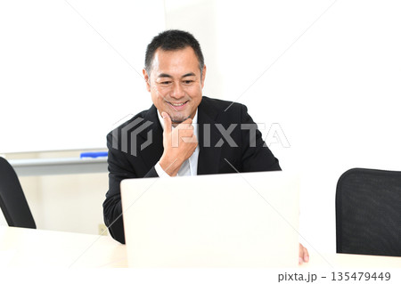 ノートPCを見る笑顔のスーツ姿の中年男性 135479449