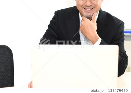 ノートPCを見る笑顔のスーツ姿の中年男性 135479450