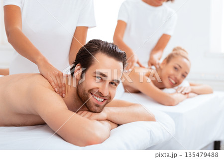 Joyful Couple Receiving Neck Massage Lying Together At Spa Beauty Center. Happy Spouses Relaxing While Masseuses Massaging Their Bodies. Romantic Spa Vacation Concept. Selective Focus Joyful Couple Receiving Neck Massage Lying Together At Spa Beauty Center. Happy Spouses Relaxing While Masseuses Massaging Their Bodies. Romantic Spa Vacation Concept. Selective Focus 135479488