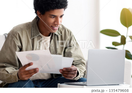 Positive black guy studying online at home, writing coursework paper or getting ready for exam. African American male student working on educational project remotely, talking to tutor on laptop Positive black guy studying online at home, writing coursework paper or getting ready for exam. African American male student working on educational project remotely, talking to tutor on laptop 135479608