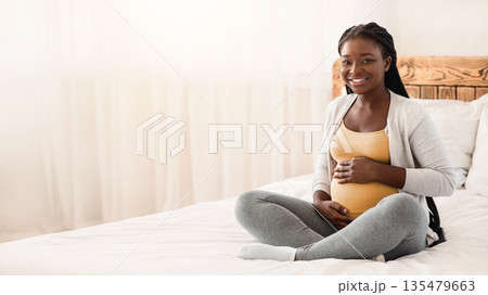 Pregnancy Time. Happy Black Pregnant Woman Sitting On Bed Touching Belly, Young Expectant Lady Posing In White Bedroom, Cuddling Tummy And Smiling At Camera, Resting At Home, Copy Space Pregnancy Time. Happy Black Pregnant Woman Sitting On Bed Touching Belly, Young Expectant Lady Posing In White Bedroom, Cuddling Tummy And Smiling At Camera, Resting At Home, Copy Space 135479663