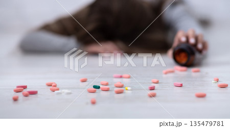 Young woman committing suicide, lying on floor with tablets scattered from jar, selective focus. Depression and drugs overuse, mental illness or psychological disorder concept Young woman committing suicide, lying on floor with tablets scattered from jar, selective focus. Depression and drugs overuse, mental illness or psychological disorder concept 135479781