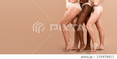 Cropped Image Of Three Multiethnic Women Posing In Underwear Over Beige Background, Bottom Part Of Multicultural Group Of Unrecognizable Ladies Wearing Lingerie Standing Together In Studio, Copy Space 135479811