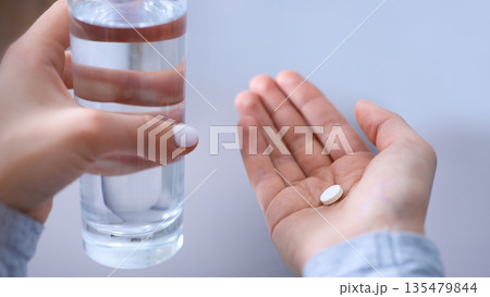 Closeup view of young woman with glass of water taking antidepressants or sleeping pills. Unrecognizable millennial lady suffering from sleep deprivation or depression, overusing medical drugs Closeup view of young woman with glass of water taking antidepressants or sleeping pills. Unrecognizable millennial lady suffering from sleep deprivation or depression, overusing medical drugs 135479844
