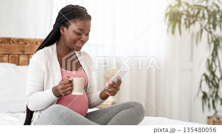 Leisure During Pregnancy. Black Expecting Lady Relaxing On Bed With Smartphone And Drinking Tea, Browsing Internet And Enjoying Hot Drink, Pregnant African Woman Resting In Bedroom At Home, Copy Space Leisure During Pregnancy. Black Expecting Lady Relaxing On Bed With Smartphone And Drinking Tea, Browsing Internet And Enjoying Hot Drink, Pregnant African Woman Resting In Bedroom At Home, Copy Space 135480056