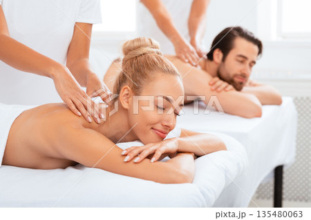 Couples Massage. Relaxed Spouses Enjoying Procedure Lying In Masseur's Chair At Spa Resort Indoor, With Eyes Closed. Romantic Beauty Wellness Treatment For Two, Massaging Therapy. Selective Focus 135480063
