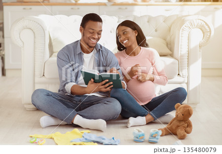 Positive African American couple making list of baby stuff for maternity hospital at home. Happy black husband and wife getting ready for birth of their child, preparing things for clinic Positive African American couple making list of baby stuff for maternity hospital at home. Happy black husband and wife getting ready for birth of their child, preparing things for clinic 135480079