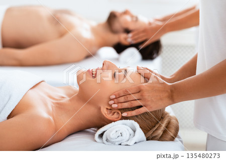 Spouses Receiving Head Massage Lying On Beds Enjoying Therapy Together, With Eyes Closed Indoor. Acupressure Massage At Romantic Spa, Relaxation And Wellness. Selective Focus Spouses Receiving Head Massage Lying On Beds Enjoying Therapy Together, With Eyes Closed Indoor. Acupressure Massage At Romantic Spa, Relaxation And Wellness. Selective Focus 135480273