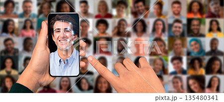 A person's hand holds a smartphone displaying a facial recognition scan of a smiling face. The background is a collage of diverse faces, showcasing modern technology in identification. A person's hand holds a smartphone displaying a facial recognition scan of a smiling face. The background is a collage of diverse faces, showcasing modern technology in identification. 135480341