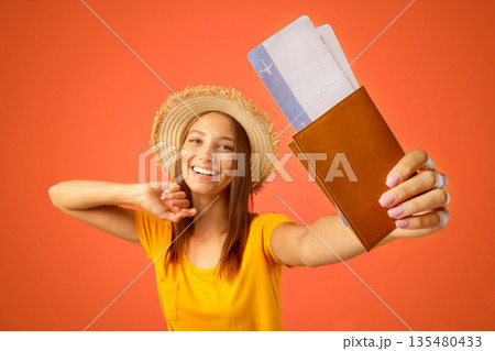 Joyful young woman in summer hat holding passport and flight tickets, yellow studio background. Happy lady traveller showing passport with plane tickets, sharing her joy with friends and followers Joyful young woman in summer hat holding passport and flight tickets, yellow studio background. Happy lady traveller showing passport with plane tickets, sharing her joy with friends and followers 135480433
