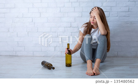 Millennial woman feeling depressed, drinking alcohol to ease emotional pain on floor at home, copy space. Young lady drowning her frustration and grief in booze. Alcoholism and mental disorders 135480562