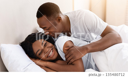 Happy loving african-american couple relaxing in bed at home, enjoying togetherness and tenderness in love, copy space. Cheerful black family man and woman in love having fun in bedroom Happy loving african-american couple relaxing in bed at home, enjoying togetherness and tenderness in love, copy space. Cheerful black family man and woman in love having fun in bedroom 135480712