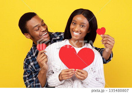 Valentines day, romantic and date. Happy young african american couple in love with hearts have fun together at spare time at covid-19 pandemic, isolated on yellow background, studio shot, copy space Valentines day, romantic and date. Happy young african american couple in love with hearts have fun together at spare time at covid-19 pandemic, isolated on yellow background, studio shot, copy space 135480807