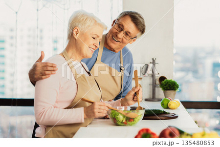 Side View Of Happy Senior Spouses Cooking Together In Modern Kitchen At Home. Elderly Husband And Wife Making Healthy Salad For Dinner Standing Indoors. Nutrition and family recipes Side View Of Happy Senior Spouses Cooking Together In Modern Kitchen At Home. Elderly Husband And Wife Making Healthy Salad For Dinner Standing Indoors. Nutrition and family recipes 135480853