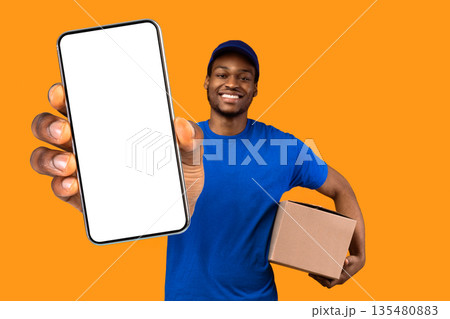 Best Delivery Service Concept. Smiling black male courier wearing blue cap and uniform holding cardboard box and showing thumbs up gesture standing isolated over yellow orange studio background Best Delivery Service Concept. Smiling black male courier wearing blue cap and uniform holding cardboard box and showing thumbs up gesture standing isolated over yellow orange studio background 135480883