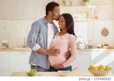 Maternity and healthy eating concept. Caring black husband kissing his pregnant wife in kitchen while cooking breakfast. Expectant African American couple having romantic moment at home Maternity and healthy eating concept. Caring black husband kissing his pregnant wife in kitchen while cooking breakfast. Expectant African American couple having romantic moment at home 135480925