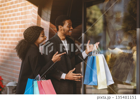 Wow, amazing clothes and low price during Black Friday and final sale. Surprised smiling young african american family with many colored packages show on showcase with huge discount, free space 135481151