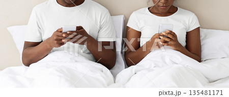 Unrecognizable black couple using smartphones in bed before sleeping, panorama. Social media addiction concept. African american family man and woman with mobile phones sitting in bed, cropped Unrecognizable black couple using smartphones in bed before sleeping, panorama. Social media addiction concept. African american family man and woman with mobile phones sitting in bed, cropped 135481171