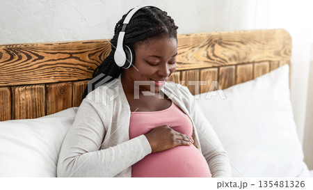 Pregnancy Music. Happy Black Pregnant Woman In Wireless Headphones Relaxing On Bed, Smiling African American Expectant Mother Touching Her Belly, Enjoying Favorite Melodies While Resting At Home Pregnancy Music. Happy Black Pregnant Woman In Wireless Headphones Relaxing On Bed, Smiling African American Expectant Mother Touching Her Belly, Enjoying Favorite Melodies While Resting At Home 135481326