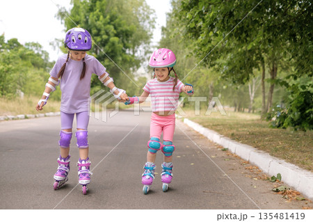 Two children learn to skate roller skating hand in hand. The sisters are happy to play sports in the summer 135481419