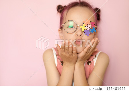 A girl wearing eyeglasses with an ornament on the lens made of pieces of colored puzzles as a sign of support for children with autism spectrum disorder 135481423