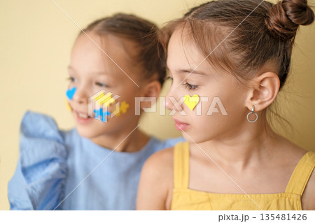 A girl with down syndrome with yellow-blue puzzles on face next to her thoughtful sister 135481426