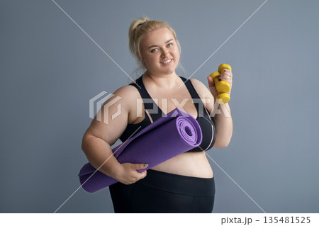 An obese fat woman with a fitness mat and dumbbells. A happy plus-size girl hoping to lose weight. World Obesity Day An obese fat woman with a fitness mat and dumbbells. A happy plus-size girl hoping to lose weight. World Obesity Day 135481525