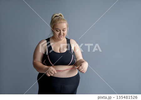 An obese woman measures her waist with a tape measure. Positive weight loss results An obese woman measures her waist with a tape measure. Positive weight loss results 135481526