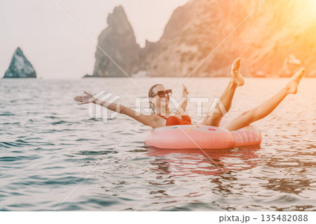 Woman, floating, donut. Joyful woman floats on inflatable donut in open sea with rocky cliffs, enjoying summer leisure. Woman, floating, donut. Joyful woman floats on inflatable donut in open sea with rocky cliffs, enjoying summer leisure. 135482088