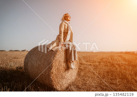 Woman Sitting on a Hay Bale in a Field 135482119