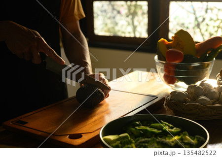 Cropped shot Man slicing avocado on a wooden board in a kitchen Cropped shot Man slicing avocado on a wooden board in a kitchen 135482522