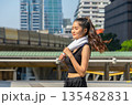 Young woman in sporty black with white towel around neck running in urban city outdoor 135482831