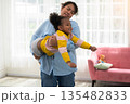 Joyful mother and daughter bonding in living room as mother lifts laughing child playfully in air like airplane at home 135482833