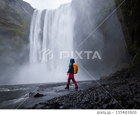 Vertical shot of hiker getting wet enjoying views on big waterfall in front of him, Iceland 135483920
