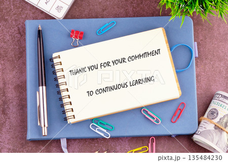 A thank you note is displayed on top of a blue notebook surrounded by a pen, money, paper clips, calculator, and plant, showing appreciation for continuous learning 135484230