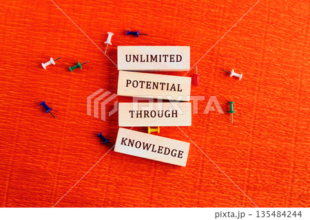 Four stacked blocks display the message unlimited potential through knowledge, surrounded by colorful push pins. The setting is on a textured orange surface 135484244