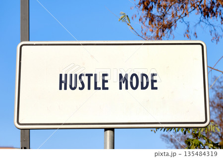 A rectangular white sign proclaims Hustle Mode in bold, dark lettering. The sign is mounted on a metal pole outdoors with a clear blue sky and trees in the background 135484319