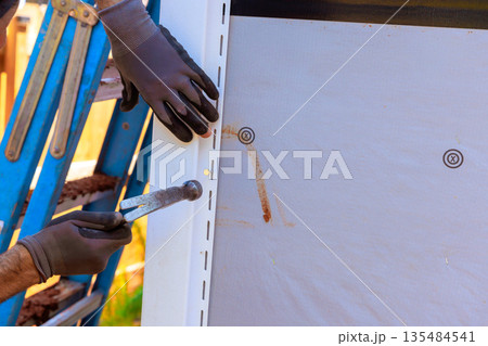 Workers install PVC siding on building beside ladder during construction Workers install PVC siding on building beside ladder during construction 135484541