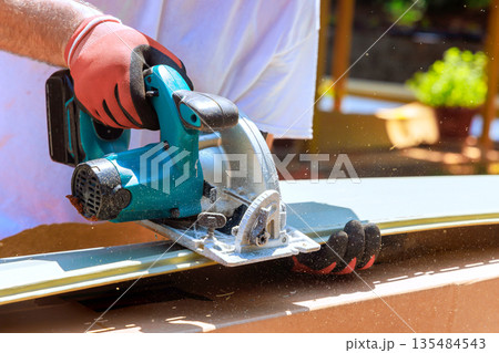 Worker uses circular saw to cut vinyl siding in construction area 135484543