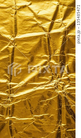 A vibrant macro texture of shimmering gold foil paper showcases intricate crinkles and reflective metallic folds, creating an abstract and luxurious background. 135485471