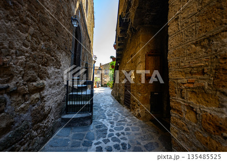Picturesque medieval-style passageway with stone paving, stairs, and warm sunlight. Authentic old town atmosphere with no people. 135485525