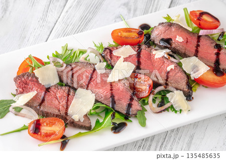 Italian beef tagliata salad with arugula and balsamic glaze on white plate 135485635
