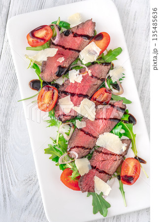 Italian beef tagliata salad with arugula and balsamic glaze on white plate Italian beef tagliata salad with arugula and balsamic glaze on white plate 135485636