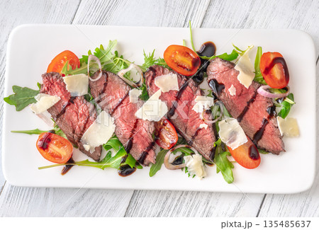 Italian beef tagliata salad with arugula and balsamic glaze on white plate Italian beef tagliata salad with arugula and balsamic glaze on white plate 135485637