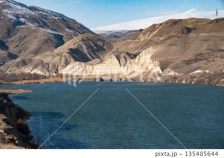 Shamb reservoir stretches between dry grassy shores and rugged mountains, blue water contrasts with warm earthy tones of the landscape Shamb reservoir stretches between dry grassy shores and rugged mountains, blue water contrasts with warm earthy tones of the landscape 135485644