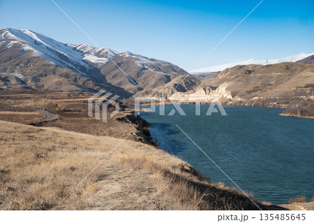 Shamb reservoir stretches between dry grassy shores and rugged mountains, blue water contrasts with warm earthy tones of the landscape 135485645