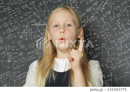 Smart school child girl standing in classroom on blackboard background. Education concept Smart school child girl standing in classroom on blackboard background. Education concept 135485775