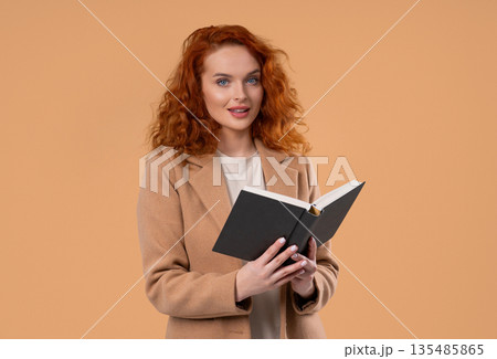 Ginger businesswoman or student reading book with smile on beige. Discovery time 135485865
